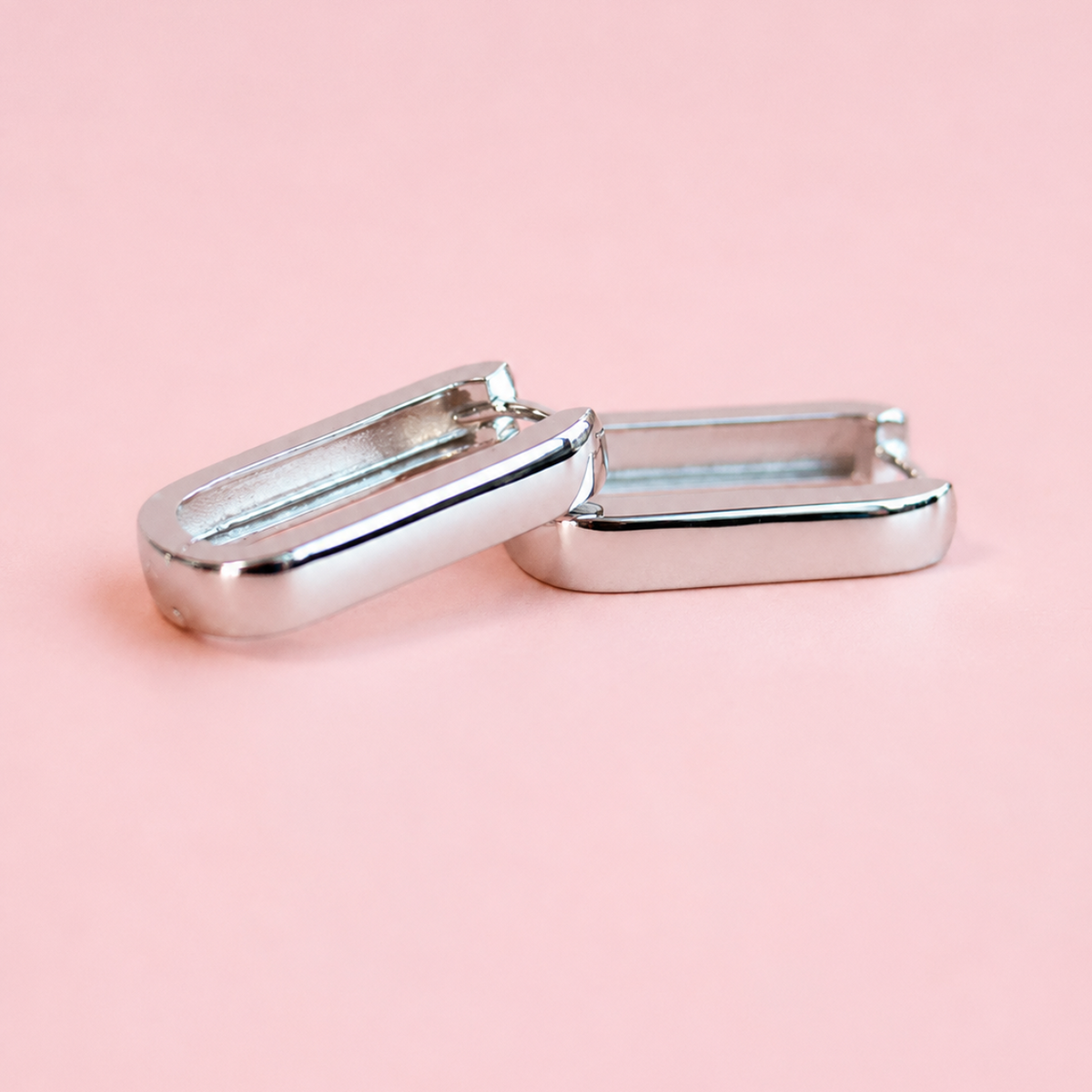 A pair of silver-toned metal capsule earrings on a solid light pink background.
