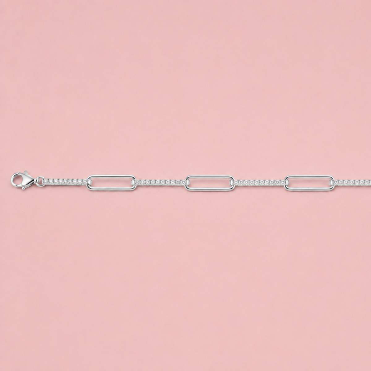 A silver paperclip chain bracelet with a lobster clasp, laid horizontally on a solid light pink background.