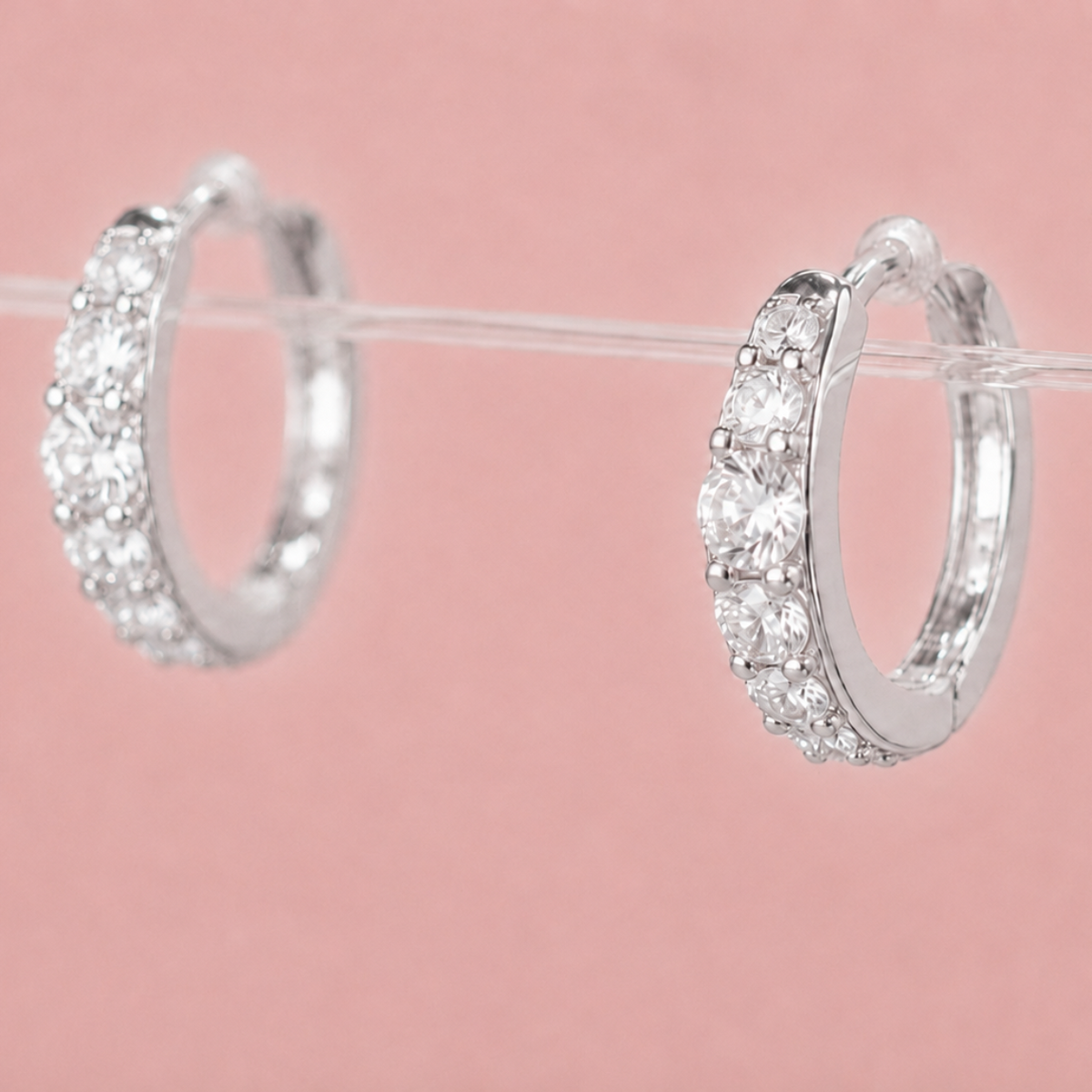 A pair of silver huggie hoop earrings set with clear pavé gemstones,