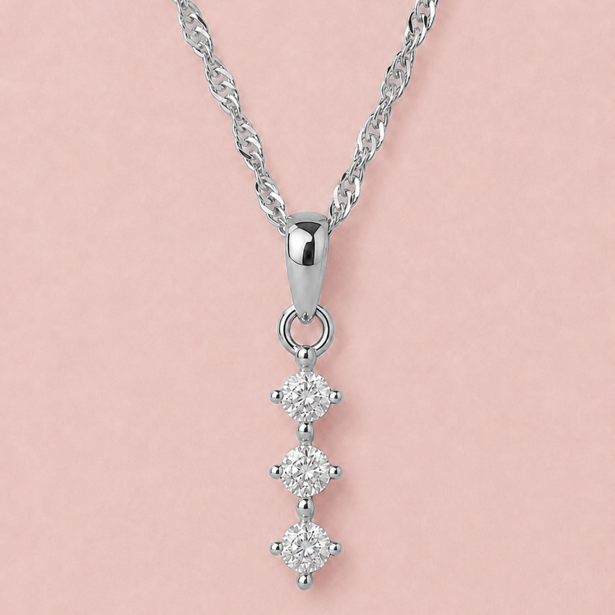 A silver necklace with a twisted chain and a vertical pendant featuring three small round-cut clear gemstones in silver settings, displayed against a solid pale pink background.