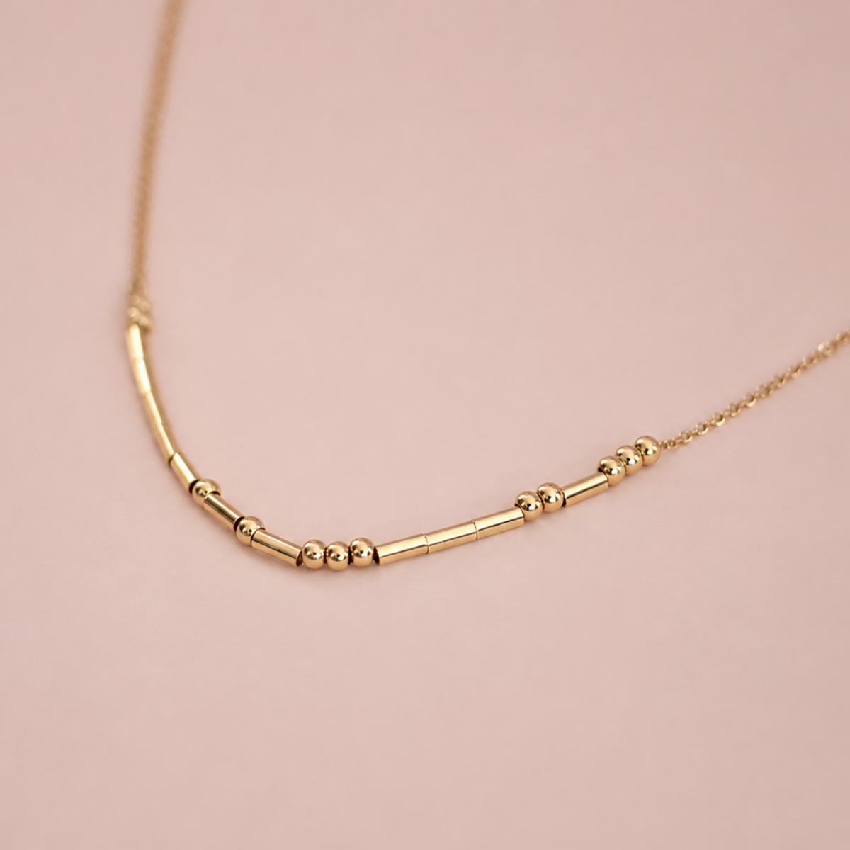 A delicate gold chain necklace featuring a central bar with small bead accents.