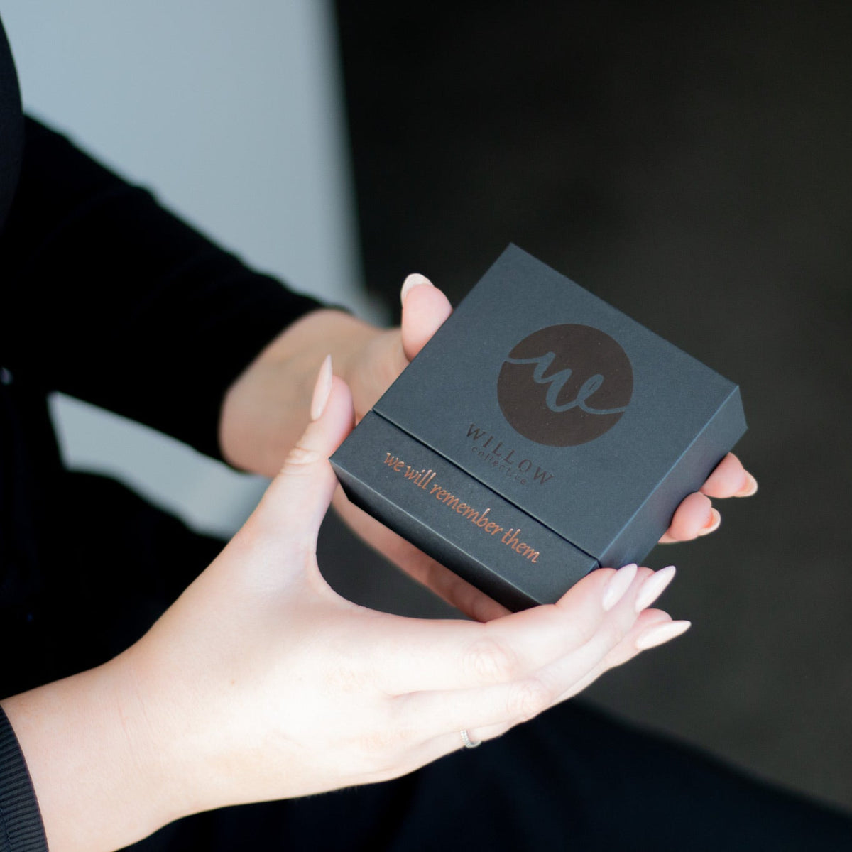 Person holding a black box with a logo on it against a dark background