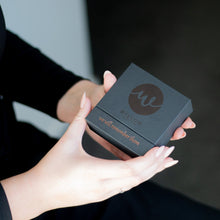 Load image into Gallery viewer, Person holding a black box with a logo on it against a dark background
