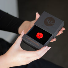 Load image into Gallery viewer, Person holding a black jewelry box with a red flower-shaped object inside, branded 'W'.
