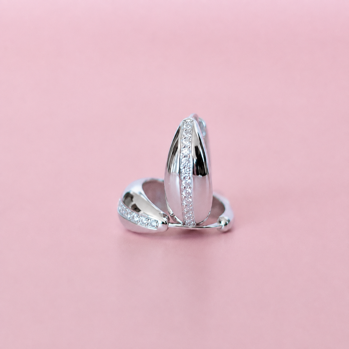 Silver huggies with clear pavé stones, photographed on a solid pink background.