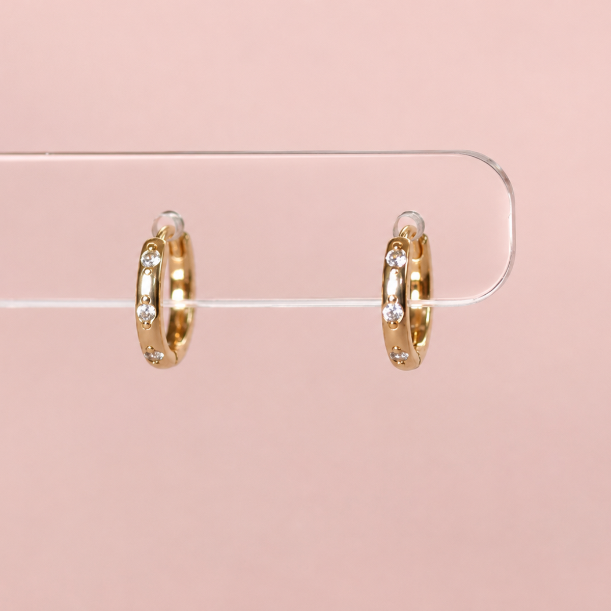 A pair of small gold huggie earrings with clear stones.